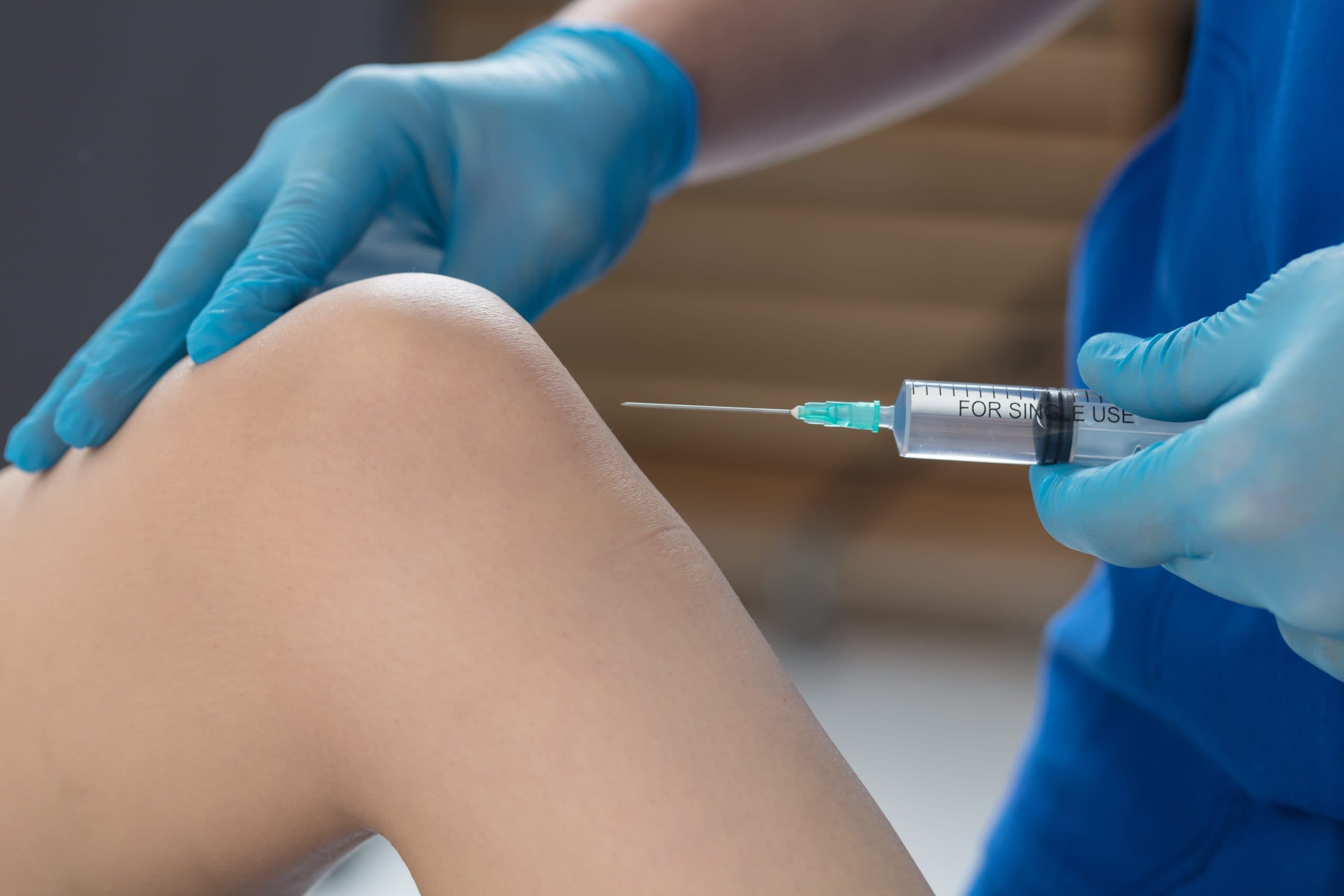 Needle positioned near knee with blue gloves