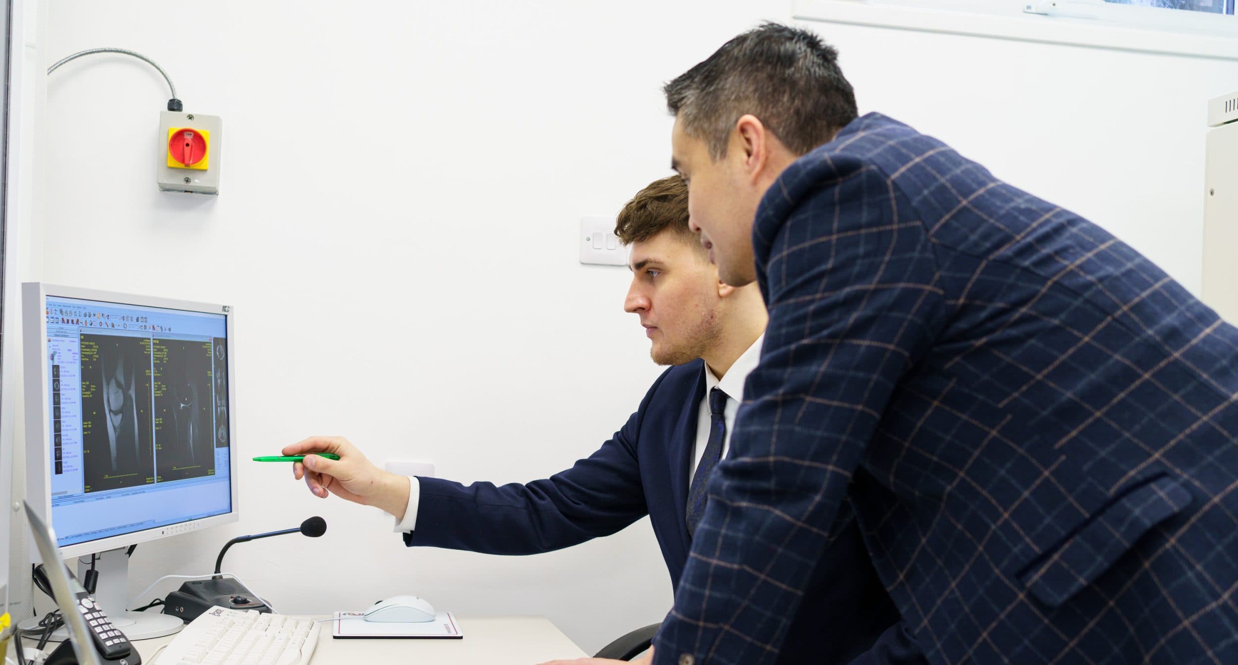Two clinicians reviewing knee MRI on desktop monitor
