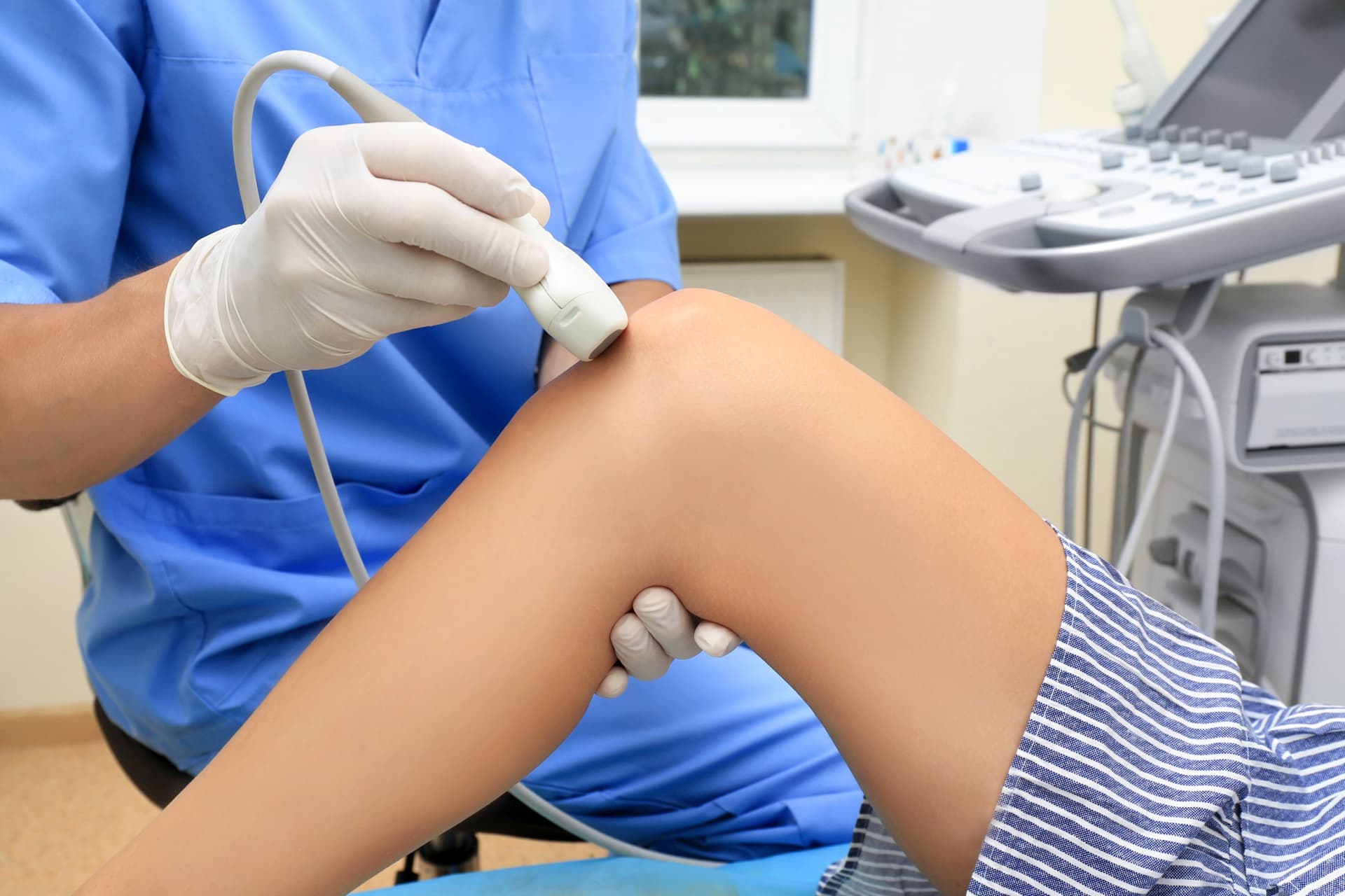 Clinician performing ultrasound knee examination during a safety-focused consultation